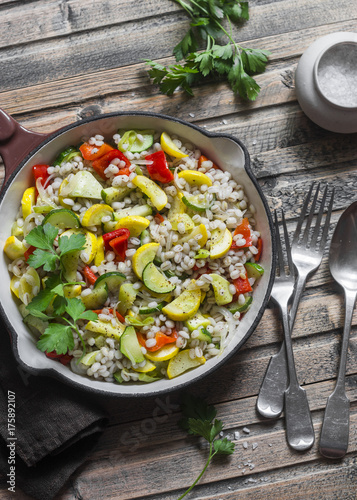 Pearl barley with seasonal garden vegetables in pan on wooden background, top view. Zucchini, sweet pepper, squash and barley stew. Vegetarian food concept