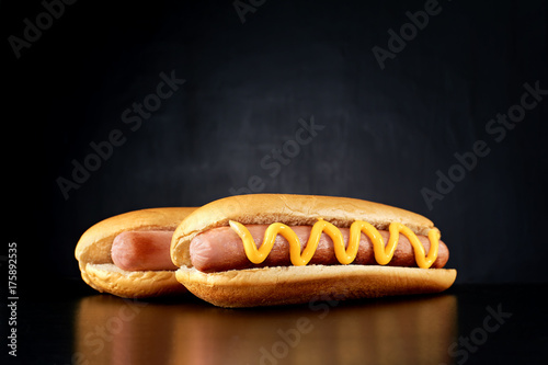 Two hotdogs with big sausage and mustard isolated on black background. Front view.