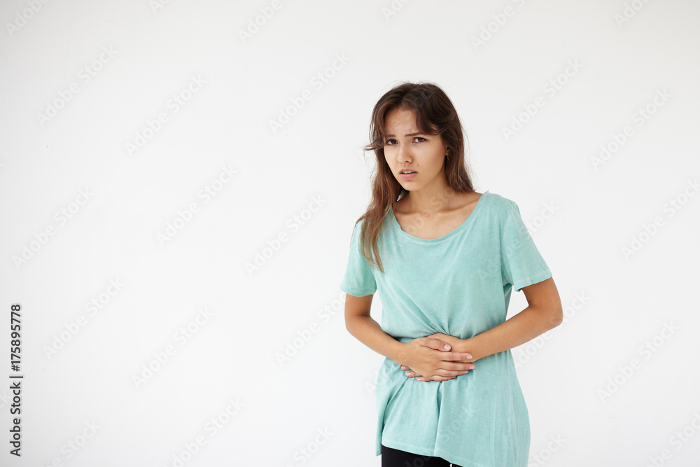 Frustrated young female having mournful painful look keeping hands on her belly, having periods, suffering from cramp. Mixed race girl having stomach ache after she ate exotic food during vacations Frustrated young female having mournful painful look keeping hands on her belly, having periods, suffering from cramp. Mixed race girl having stomach ache after she ate exotic food during vacations