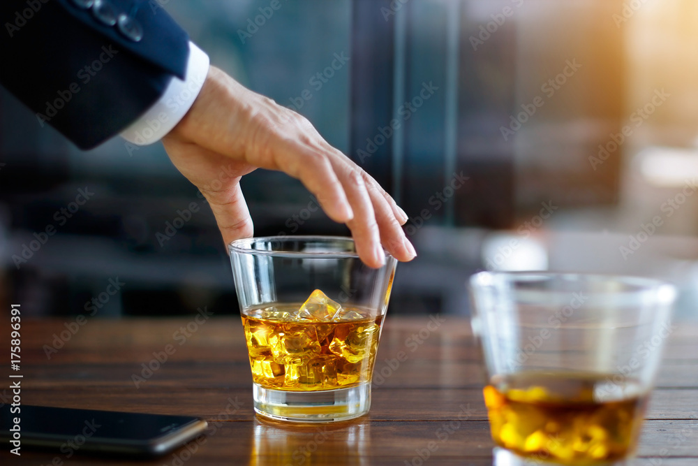 Businessman hand touching bourbon whiskey glass on wooden table in building background Businessman hand touching bourbon whiskey glass on wooden table in building background