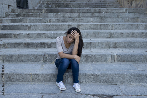 beautiful and sad Hispanic woman desperate and depressed sitting on urban city street staircase