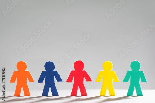 Group of Multi Colored Little People in a row on Grey Background