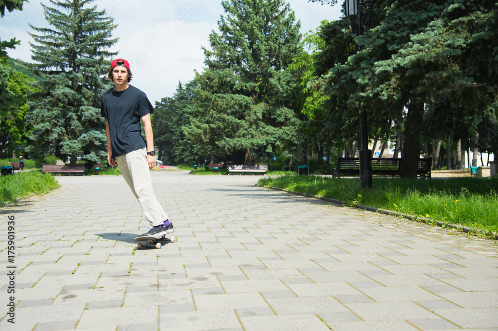 Fototapeta premium Long-haired skater-teenager in a T-shirt and a sneaker hat jumps an alley against a stormy sky