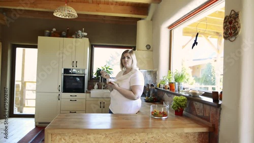 Overweight woman at home eating vegetable salad in the kitchen. photo