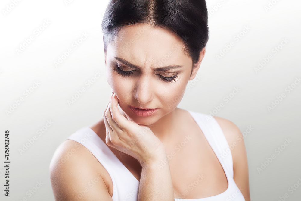 Toothache in a young beautiful woman. Caries. A woman holds her hand in the teeth area. A painful sensation. The concept of health. On a gray background. Toothache in a young beautiful woman. Caries. A woman holds her hand in the teeth area. A painful sensation. The concept of health. On a gray background.