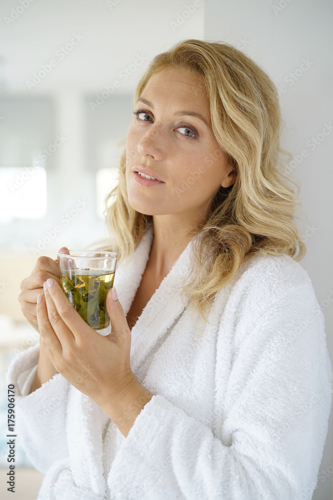 Portrait of attractive 40-year-old woman in bathrobe drinking infusion Portrait of attractive 40-year-old woman in bathrobe drinking infusion