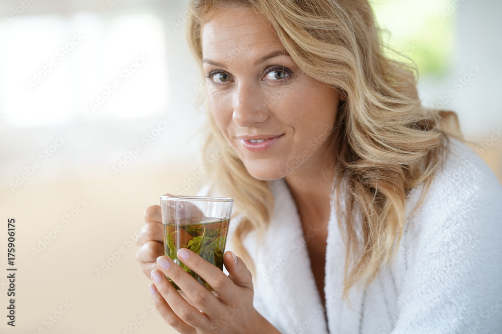 Portrait of attractive 40-year-old woman in bathrobe drinking infusion Portrait of attractive 40-year-old woman in bathrobe drinking infusion
