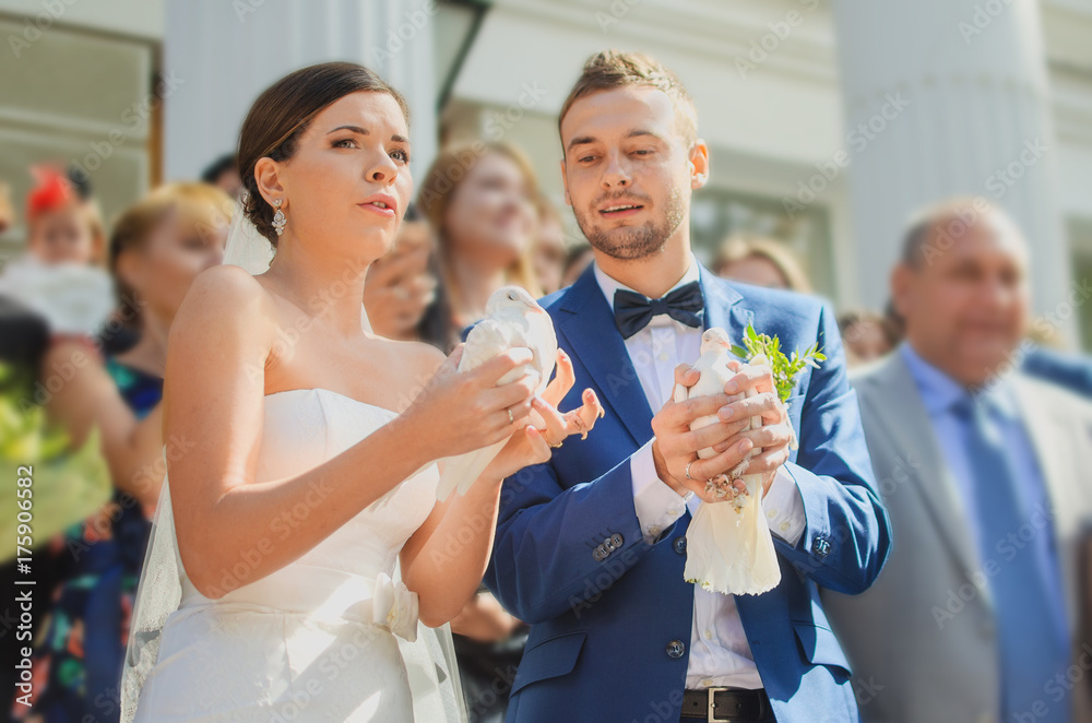 Wedding couple with pigeons at hand background wedding guests against church Wedding couple with pigeons at hand background wedding guests against church