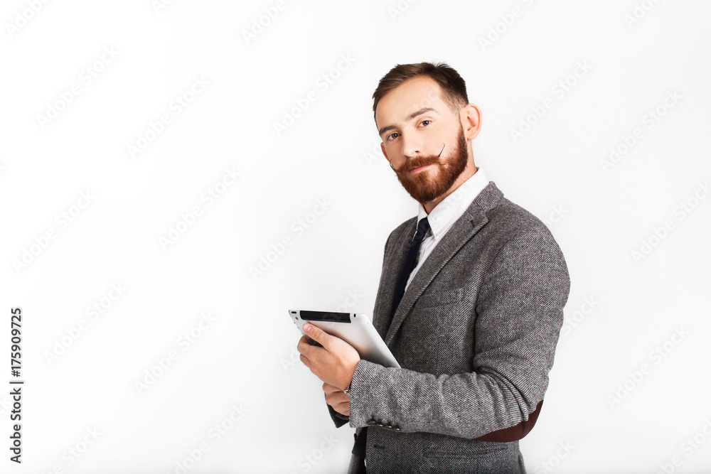 Serious man with red beard poses in grey suit with tablet in his hand Serious man with red beard poses in grey suit with tablet in his hand
