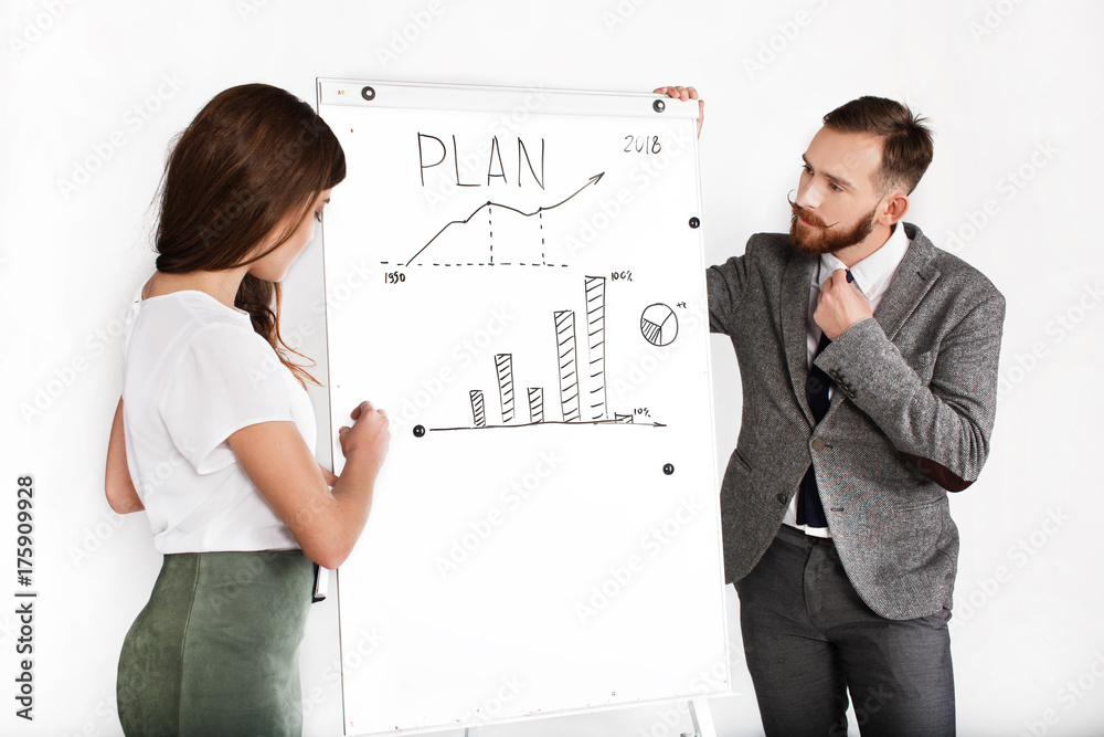 Serious man and woman discuss graph written on white board Serious man and woman discuss graph written on white board