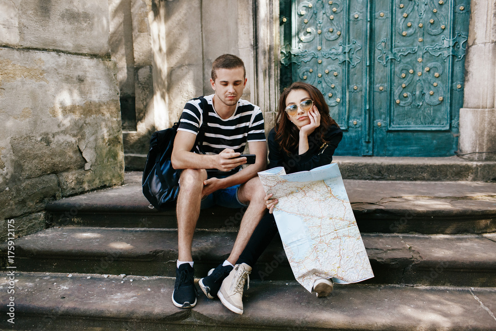 Boy and girl sit on the steps to cathedral with touristc map and watch something in the smartphone Boy and girl sit on the steps to cathedral with touristc map and watch something in the smartphone
