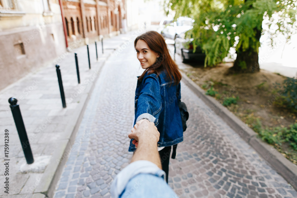 Look from behind at young woman holding man's hand in 'Follow me' pose