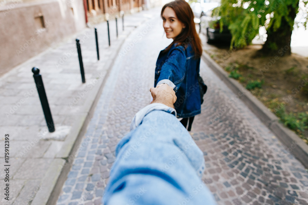 Look from behind at young woman holding man's hand in 'Follow me' pose