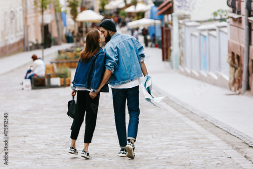 Look from behind at the couple of tourists holding their hands together while walking around the city © IVASHstudio