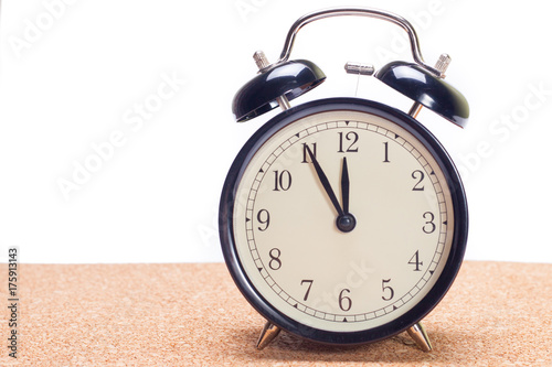 Old alarm clock on wooden table isolated white background with five minutes to twelve o'clock