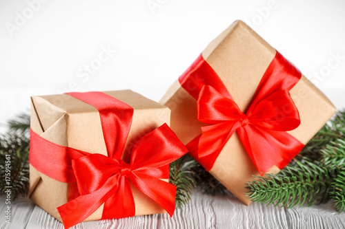 Craft gift boxes with red ribbon and bow, green Christmas tree, decorations, on white wooden background. Xmas and New Year congratulation card, banner, flyer. © Yuliia Osadcha