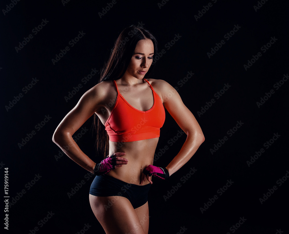 Nice sexy fitness woman showing abdominal muscles isolated over black background. Trained female body.