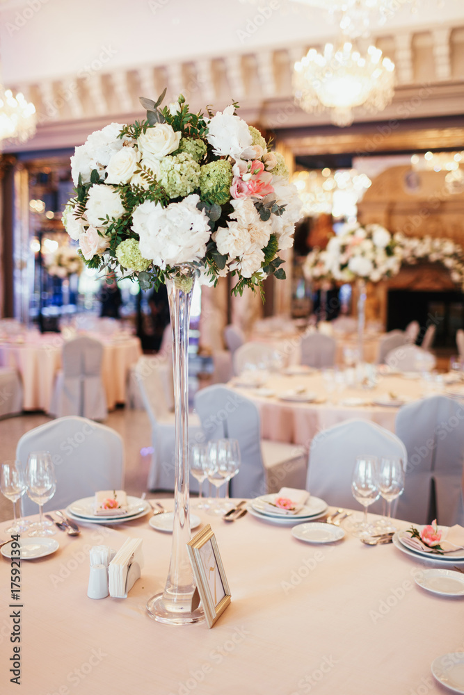 Tall vase with white and green flowers stands on round dinner table number nine