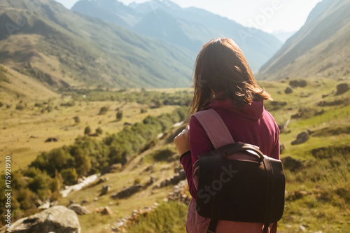 a young woman traveler with backpack enjoying view of autumn mountains, rear view