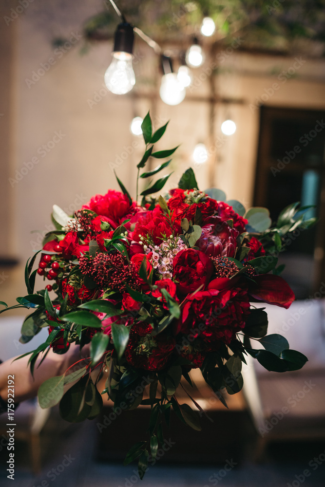 Fototapeta premium Stunning wedding bouquet made of red peonies, roses and dark green leaves