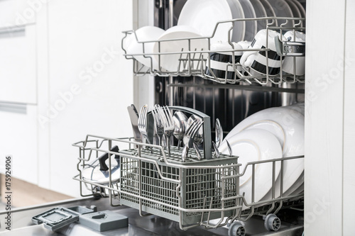 Open dishwasher with clean dishes in white kitchen photo