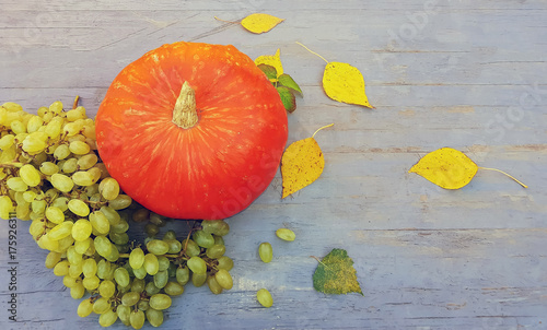 Pumpkin, grapes and autumn leaves on a wooden background.