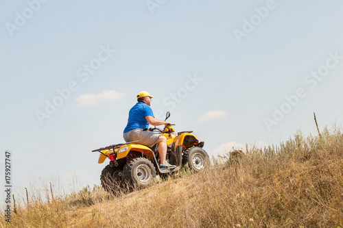 Caucasian man in sport protective goggles riding an ATV quad bike over rough terrain with meadows of dry autumn grass. Adventure activity concept