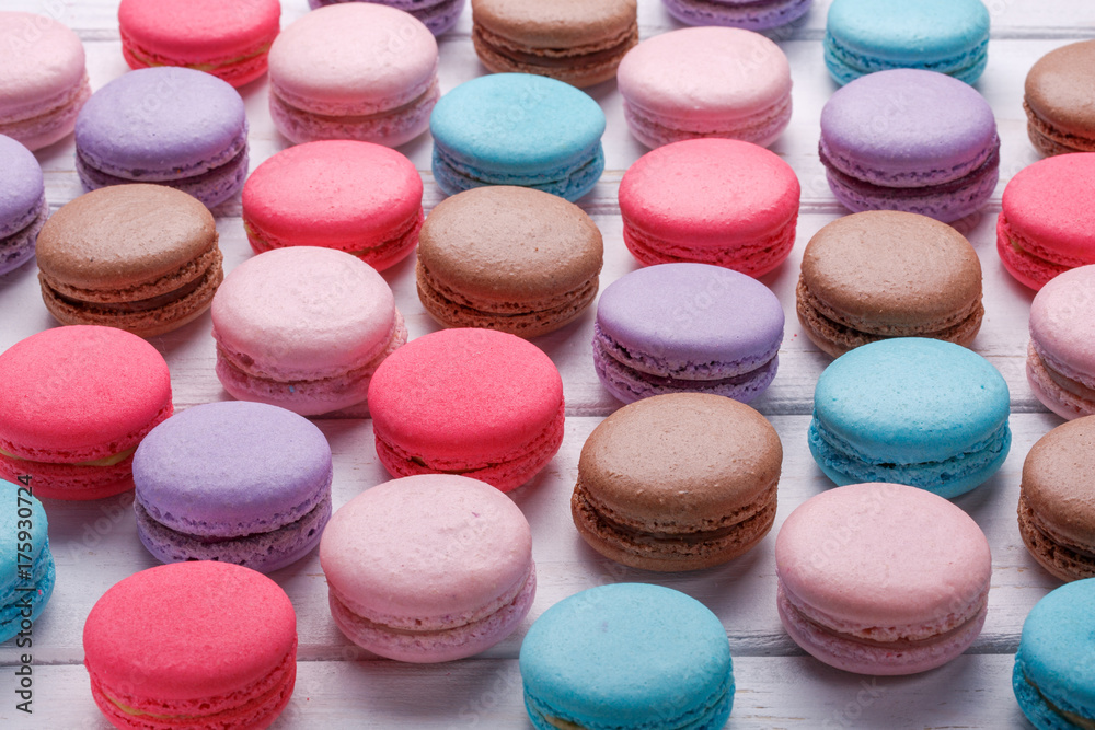 Fototapeta premium Picture of a lot of sweet colorful macaroons on white wooden background.
