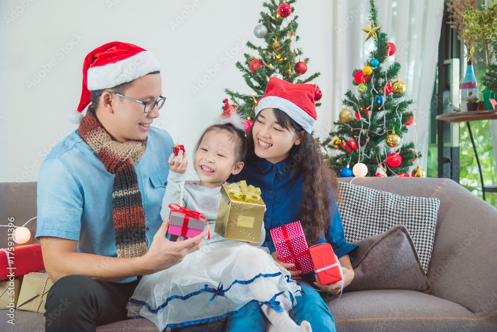 Little asian girl and her parents open christmas gifts box on sofa Little asian girl and her parents open christmas gifts box on sofa