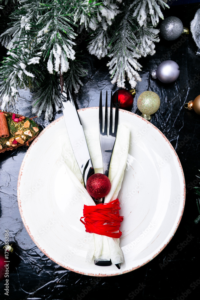 Christmas table place setting. Holidays background. White plate, knife and fork with christmas decorations on black table. Top view. Christmas table place setting. Holidays background. White plate, knife and fork with christmas decorations on black table. Top view.