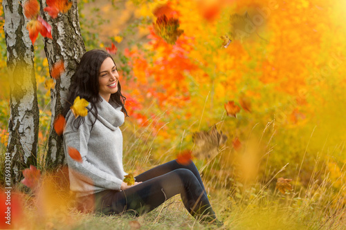Portrait of young woman with falling autumn leaves.