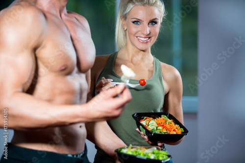 Happy couple in gym feeding each other with fresh salad at gym