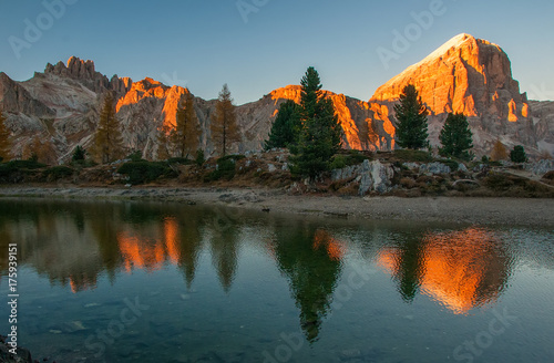 Mountain rocks and autumn trees reflected in water of Limides Lake at sunset, Dolomite Alps, Italy