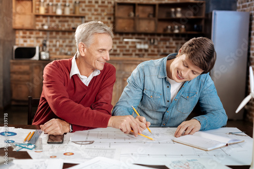 Smiling man pointing at problematic place in colleagues blueprint