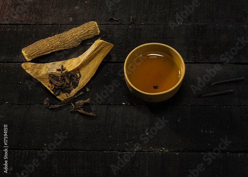 The Chinese tea cup was put beside wooden herb,on black timber wooden board,in abstract art design,vintage and art style. photo