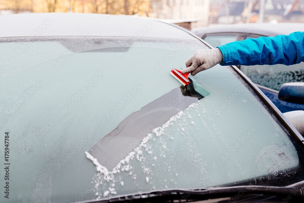 Naklejka premium Woman removing ice from car windshield with glass scraper.