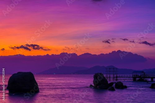 The coastal zone in the rays of a purple sunset. In the background, silhouettes of mountains are visible. End of the Earth. Hainan, China.