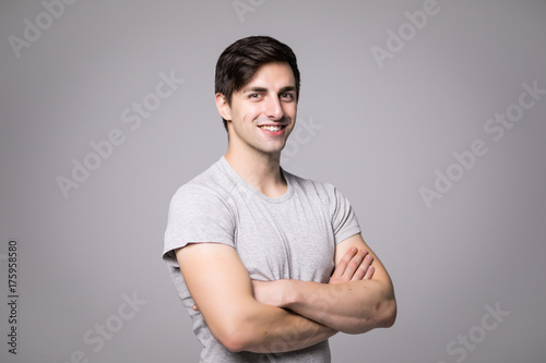 Obraz na plátně Portrait of a happy casual man standing with arms folded over gray background an