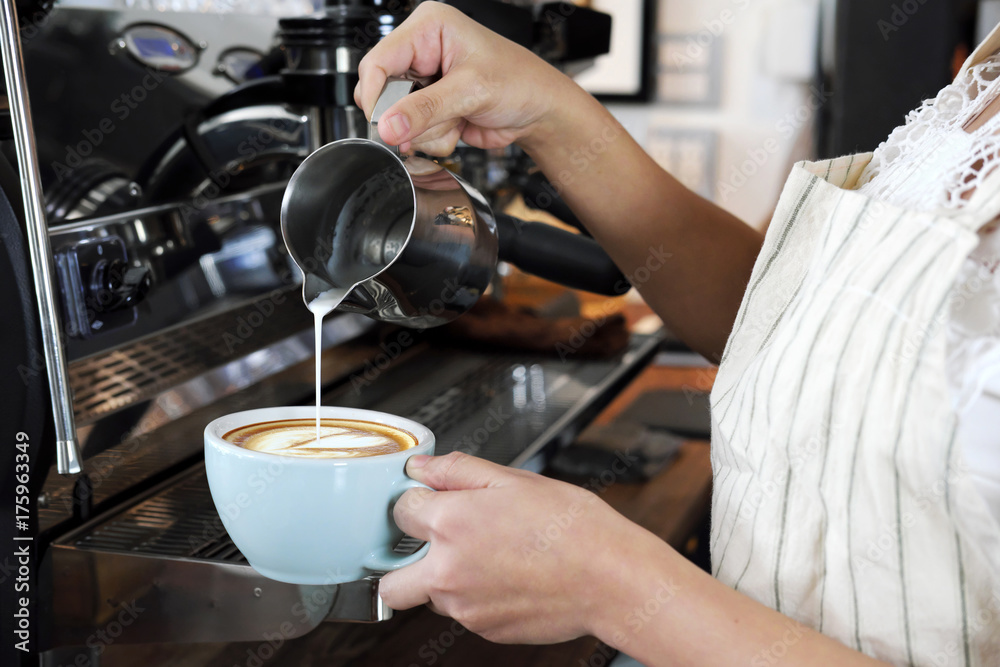 Close-up hand of barista making latte or cappucino coffee in coffee shop. Cafe restaurant service, food and drink industry concept.