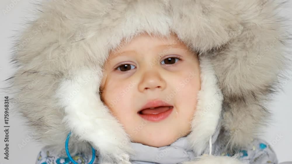 A funny happy child dressed in warm fur clothes looks at the camera, laughs and smiles. Close-up portrait. The concept of winter, frost and snow, cold weather, Cool temperature and Christmas A funny happy child dressed in warm fur clothes looks at the camera, laughs and smiles. Close-up portrait. The concept of winter, frost and snow, cold weather, Cool temperature and Christmas