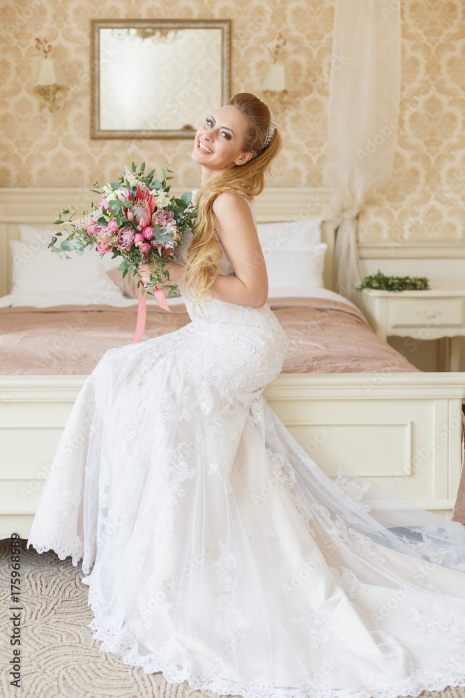 Beautiful young Bride with blonde hairs in a bedroom. Classic white wedding dress. Full-length portrait Beautiful young Bride with blonde hairs in a bedroom. Classic white wedding dress. Full-length portrait