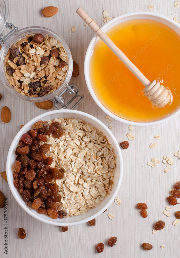Healthy Breakfast. Oatmeal with raisins in white bowl. Almonds, honey on white table background Healthy Breakfast. Oatmeal with raisins in white bowl. Almonds, honey on white table background