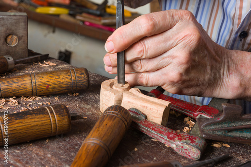 Manos de maestro tallista trabajando la madera con martillo y gubia.
