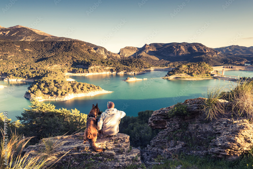 Travellers couple looking at lake from hill - obrazy, fototapety, plakaty 