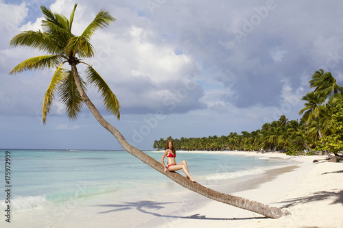 beautiful lady is sitting on the palm tree at tropical beach photo