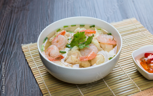 Shrimp wonton noodle soup with braised pork in soup on wooden table - Asian food style.