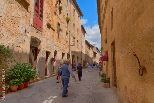 Beautiful narrow street with sunlight and flowers in the small magical and old village of Pienza, Val D'Orcia Tuscany, Italy. © djevelekova