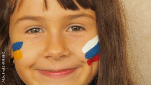 Happy child with the flag of Russia and Ukraine. A little girl with painted flags of Russia and Ukraine. photo