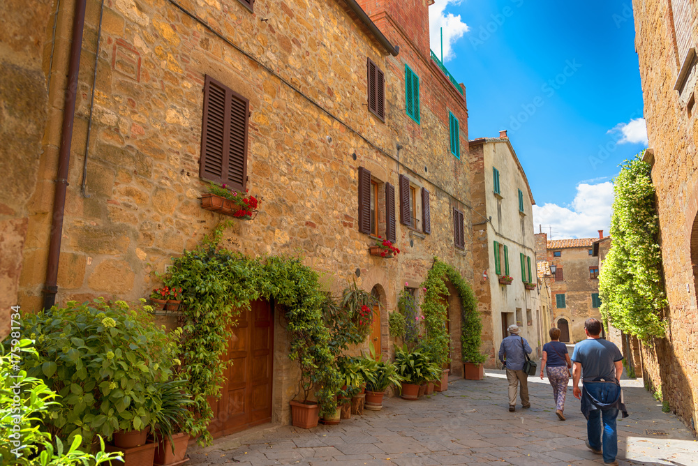 Beautiful narrow street with sunlight and flowers in the small magical and old village of Pienza, Val D'Orcia Tuscany, Italy.