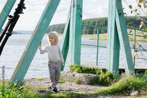 Obraz na płótnie A happy blond boy staying at an Old wooden pendant bridge - summertime activity at a country village, the Urals, Russiaf, Kuryi w salonie
